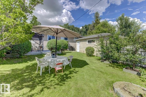 Expansive backyard featuring a manicured lawn, established perimeter trees, and a detached structure with a pitched roof - 15707 92 Avenue, Edmonton, AB 