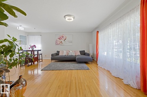 Spacious living area featuring polished wood-finish flooring, abundant natural light, a contemporary ceiling fixture, and a recessed dining nook with built-in cabinetry - 15707 92 Avenue, Edmonton, AB 