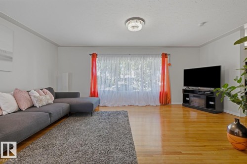 Bright living area featuring wood-finish flooring, white walls, and a large window - 15707 92 Avenue, Edmonton, AB 