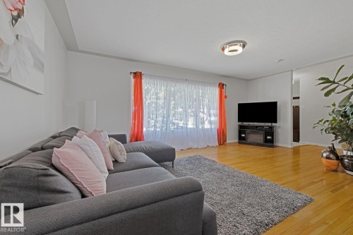 Spacious living area featuring polished wood-finish flooring, a large picture window, and a contemporary ceiling light fixture - 15707 92 Avenue, Edmonton, AB 
