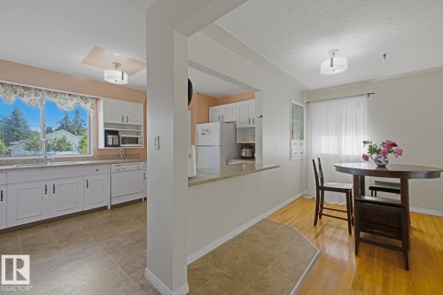 Kitchen and dining area featuring white cabinetry, light-toned countertops, a dishwasher, and a large window - 15707 92 Avenue, Edmonton, AB 