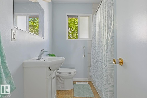 Bathroom featuring a white vanity with integrated sink, chrome faucet, wall-mounted mirror, and a window for natural light - 15707 92 Avenue, Edmonton, AB 