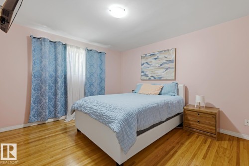 Bedroom featuring wood-finish flooring, light-colored walls, and a window with sheer and patterned drapes - 15707 92 Avenue, Edmonton, AB 
