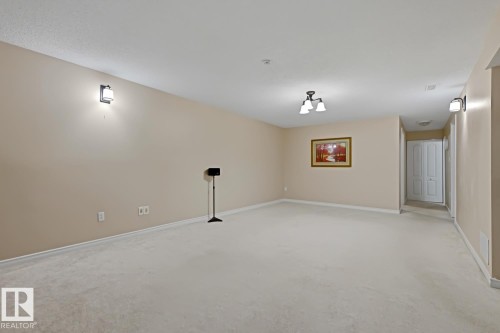 Spacious interior room featuring light-toned carpeting, neutral wall paint, and white baseboards - 15707 92 Avenue, Edmonton, AB 