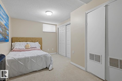 Carpeted room featuring a ceiling-mounted light fixture, a window with a roller shade, and two white bi-fold closet doors - 15707 92 Avenue, Edmonton, AB 