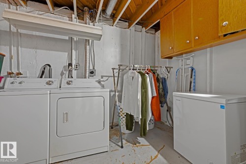 Dedicated laundry area featuring a white washer and dryer set, overhead wood-finish cabinetry, and a chest freezer - 15707 92 Avenue, Edmonton, AB 