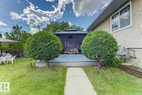 Backyard patio featuring a covered gazebo, concrete pathway, two mature topiary shrubs, and a stucco-finish exterior - 15707 92 Avenue, Edmonton, AB 