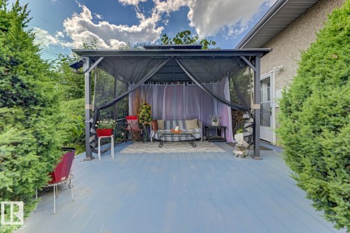 Expansive deck featuring a blue-painted surface, a gazebo with privacy screens, and surrounding evergreen shrubbery - 15707 92 Avenue, Edmonton, AB 