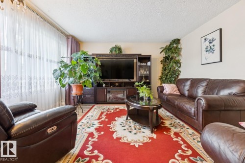 Spacious living area featuring wood-finish flooring, a decorative area rug, and a large window with sheer and solid drapes - 3015 131 Avenue, Edmonton, AB 