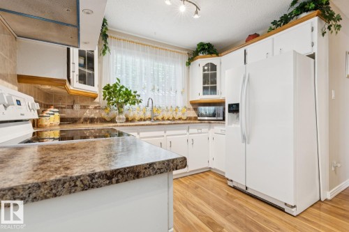 Kitchen featuring extensive white cabinetry, wood-finish flooring, stone-finish countertops, stainless-steel range hood, and a built-in microwave - 3015 131 Avenue, Edmonton, AB 