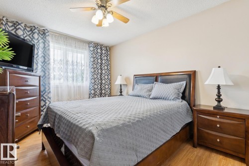 Bedroom featuring a window with sheer and patterned drapes, wood-finish flooring, a ceiling fan with integrated lighting, and neutral wall tones - 3015 131 Avenue, Edmonton, AB 