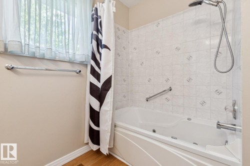 White tiled shower surround with accent tiles, a mounted shower head and hose, and a white soaking tub - 3015 131 Avenue, Edmonton, AB 