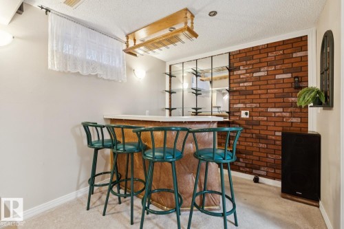 Dedicated bar area featuring a light-toned countertop, a suspended wooden glass rack, and integrated shelving with mirrored backing - 3015 131 Avenue, Edmonton, AB 
