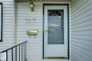 White siding exterior featuring a storm door with an arched window, brass house numbers, a coordinating brass mailbox, and a black metal handrail - 3015 131 Avenue, Edmonton, AB 