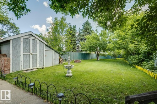 Spacious green lawn featuring a storage shed with double doors and a single side door, mature trees, a privacy fence, and decorative border fencing - 3015 131 Avenue, Edmonton, AB 