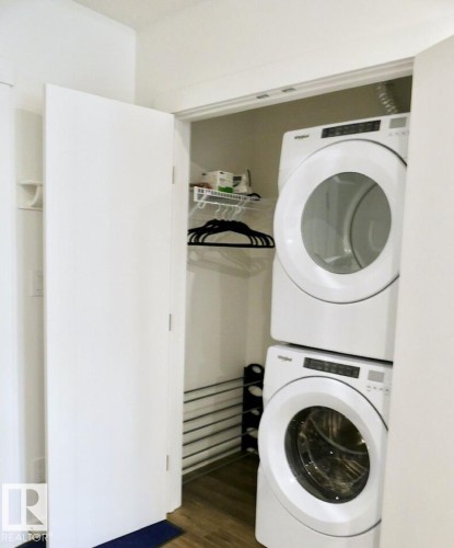 Dedicated laundry closet featuring a stacked washer and dryer, wood-finish flooring, and a wire storage shelf - 216 11503 76 Avenue, Edmonton, AB 