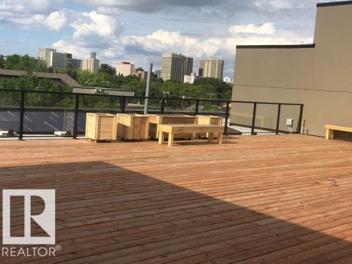 Rooftop solar panel array on a flat roof, complemented by a distant cityscape and abundant green tree canopy - 216 11503 76 Avenue, Edmonton, AB 