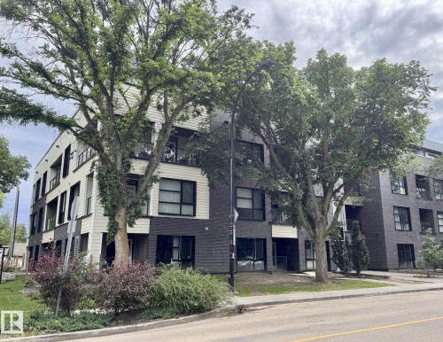 Contemporary multi-story building featuring a dark brick facade, expansive windows, glass balconies, and a central glass-enclosed stairwell - 216 11503 76 Avenue, Edmonton, AB 