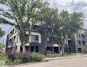 Contemporary multi-story building featuring a dark brick facade, expansive windows, glass balconies, and a central glass-enclosed stairwell - 216 11503 76 Avenue, Edmonton, AB 
