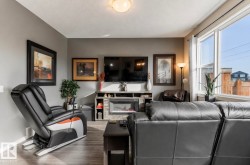 Living area featuring wood-finish flooring, a built-in electric fireplace with stone-look surround and media console, and a large window - 