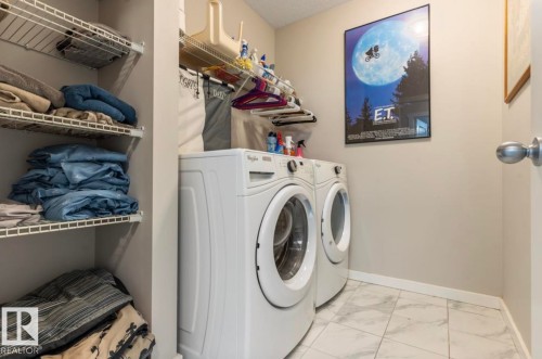 Dedicated laundry area featuring front-loading appliances, white wire shelving, and light-toned tile flooring - 12737 205 Street Nw, Edmonton, AB 
