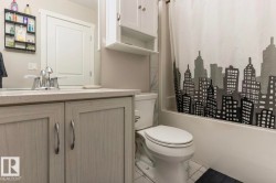 Bathroom featuring a light-toned vanity with brushed nickel hardware, a speckled countertop, and a white toilet - 