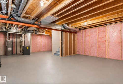Expansive unfinished lower level featuring exposed wood joists, insulated perimeter walls, a utility area with water heater and furnace, and a visible stairwell - 12737 205 Street Nw, Edmonton, AB 