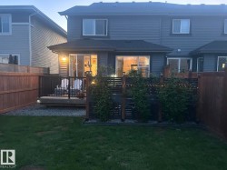 Rear exterior featuring a wooden deck with black railing, privacy fencing, and a manicured lawn - 
