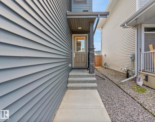 Front entry with concrete steps and landing, featuring a covered porch with a stone-accented pillar - 12737 205 Street Nw, Edmonton, AB 