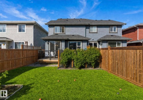 Landscaped backyard featuring a wooden privacy fence, a wooden deck with black railings, and a manicured lawn - 12737 205 Street Nw, Edmonton, AB 