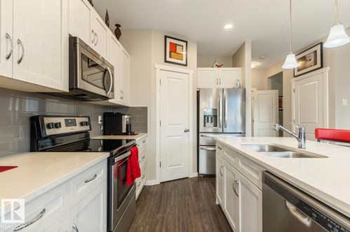 Contemporary kitchen featuring white cabinetry with silver hardware, stainless steel appliances, light-toned countertops, a subway tile backsplash, and wood-finish flooring - 12737 205 Street Nw, Edmonton, AB 