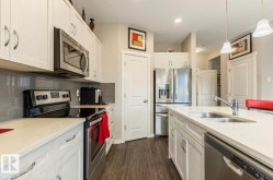 Contemporary kitchen featuring white cabinetry with silver hardware, stainless steel appliances, light-toned countertops, a subway tile backsplash, and wood-finish flooring - 