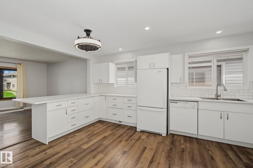 Modern kitchen featuring white cabinetry, light-toned countertops, subway tile backsplash, and wood-finish flooring - 9545 65 Avenue, Edmonton, AB 