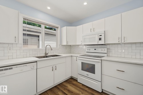 Bright kitchen featuring white cabinetry, subway tile backsplash, white countertops, stainless steel double basin sink, and wood-finish flooring - 9545 65 Avenue, Edmonton, AB 