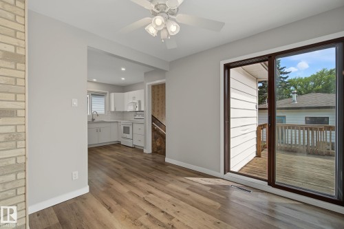 Open-concept living area featuring wood-finish flooring, a contemporary ceiling fan with integrated lighting, and a sliding glass door leading to an outdoor deck with wooden railings - 9545 65 Avenue, Edmonton, AB 