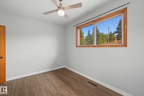 Spacious room featuring wood-finish flooring, a large window with a natural wood frame, and a ceiling fan with integrated lighting - 9545 65 Avenue, Edmonton, AB 