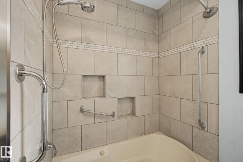 Bathtub with light-toned wall tiling, contrasting mosaic accent tile, built-in shower niches, and chrome grab bars - 9545 65 Avenue, Edmonton, AB 