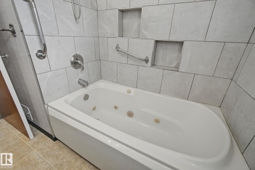 Jetted soaking tub with chrome fixtures, surrounded by light-toned rectangular wall tiles - 9545 65 Avenue, Edmonton, AB 