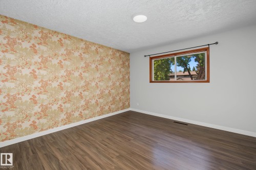 Room featuring wood-finish flooring, a decorative accent wall, a window with a wood frame, a ceiling-mounted light fixture, and white baseboards - 9545 65 Avenue, Edmonton, AB 