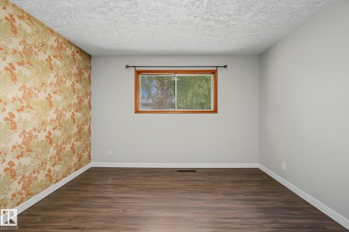 Room featuring wood-finish flooring, a decorative accent wall, a window with a wood frame, and a textured ceiling - 9545 65 Avenue, Edmonton, AB 