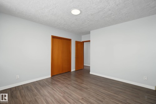 Spacious room featuring wood-finish flooring, light gray walls, white baseboards, and a flush-mount ceiling light fixture - 9545 65 Avenue, Edmonton, AB 