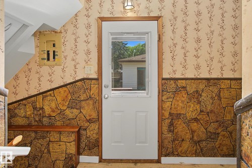 Entryway featuring a white door with an integrated window, wood-finish trim, and a stone-look wainscoting - 9545 65 Avenue, Edmonton, AB 