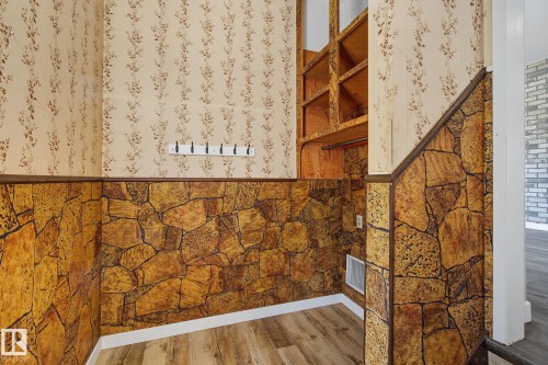 Room featuring wood-finish flooring, stone-patterned wall paneling, and an integrated shelving unit - 9545 65 Avenue, Edmonton, AB 