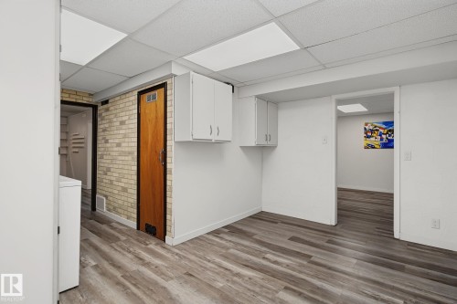 Finished lower-level space featuring wood-finish flooring, drop ceiling with integrated lighting, and white wall cabinetry - 9545 65 Avenue, Edmonton, AB 