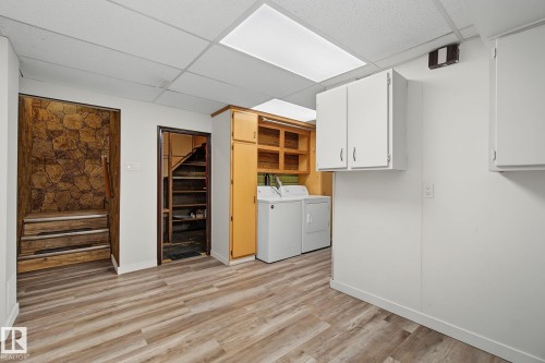 Utility space featuring wood-finish flooring, drop ceiling with integrated lighting, built-in shelving, and white cabinetry - 9545 65 Avenue, Edmonton, AB 