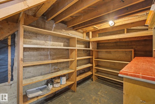 Basement utility space featuring exposed wood joists, concrete walls, built-in shelving, a utility counter, and overhead lighting - 9545 65 Avenue, Edmonton, AB 