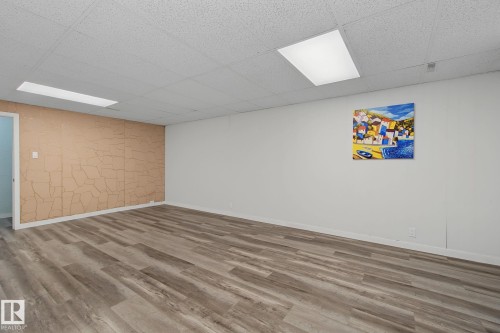 Spacious room featuring wood-finish flooring, a textured accent wall, and a drop ceiling with integrated rectangular lighting fixtures - 9545 65 Avenue, Edmonton, AB 