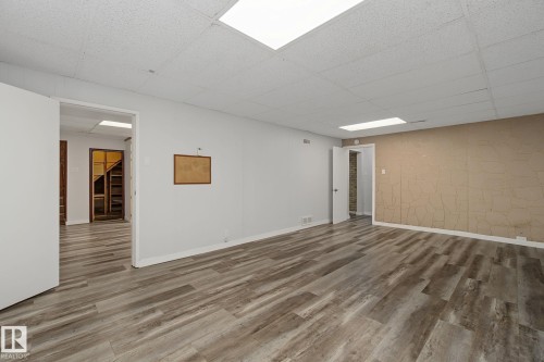 Spacious room with wood-finish flooring, drop ceiling with integrated lighting, and neutral wall tones - 9545 65 Avenue, Edmonton, AB 