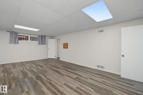 Spacious room featuring wood-finish flooring, white walls, and a drop ceiling with recessed lighting - 9545 65 Avenue, Edmonton, AB 