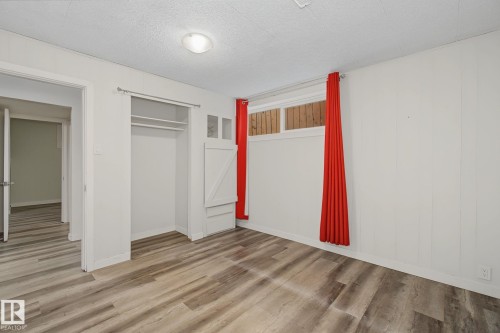 Room featuring wood-finish flooring, a built-in closet with shelving and hanging rods, and a window with a valance - 9545 65 Avenue, Edmonton, AB 